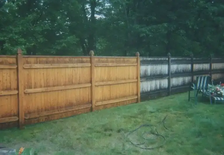 Wooden and black fencing along a grassy yard with trees in the background