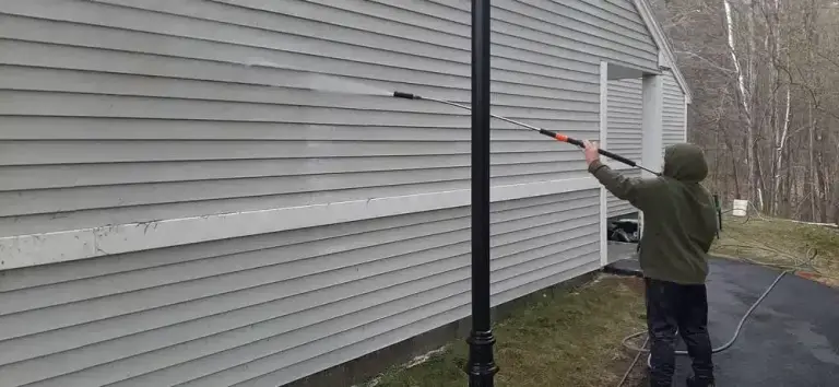 Person using a pressure washer to clean white vinyl siding on a residential house