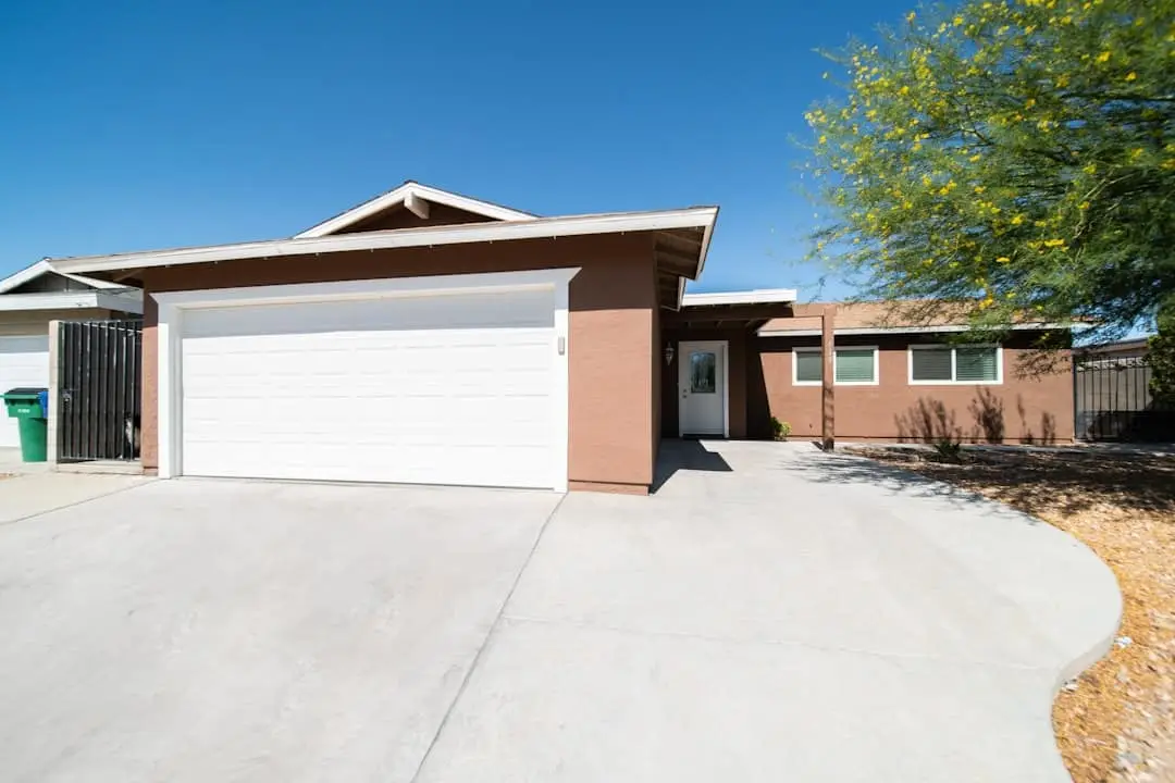 Single-story brick home with white garage door and concrete driveway under clear blue sky