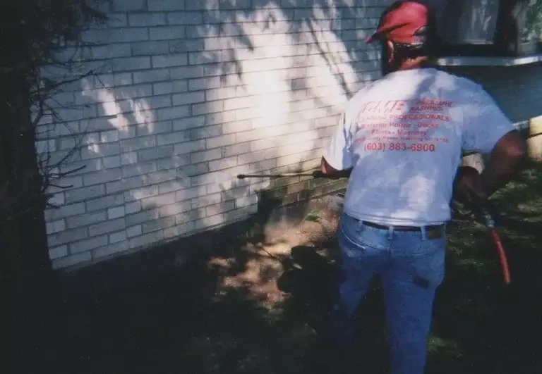Worker in red cap pressure washing vinyl siding on a residential house