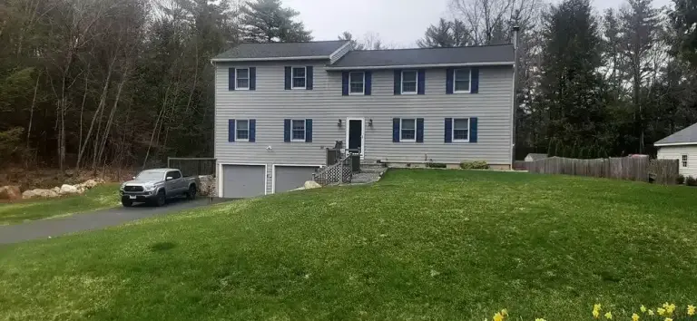 Two-story white vinyl sided house with blue shutters on a grassy lot